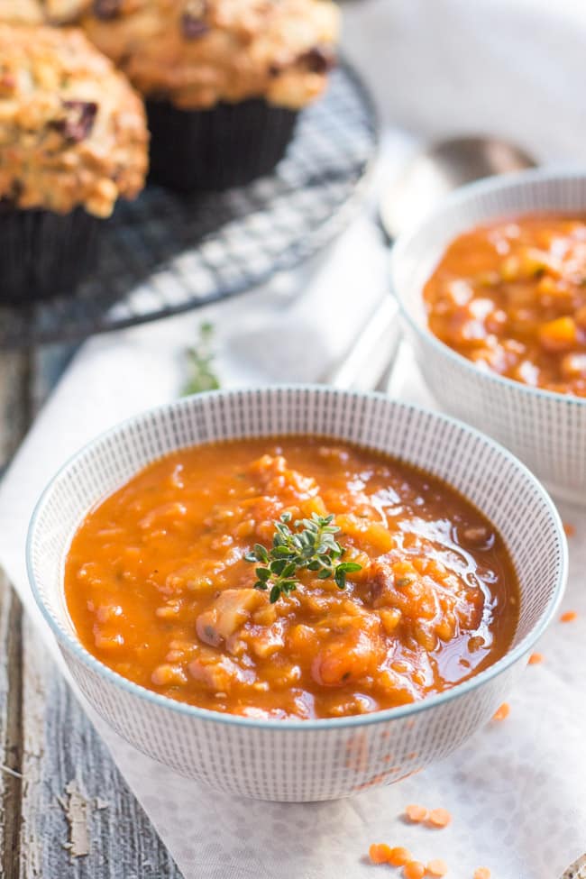 A striped bowl full of Red Lentil & Smoky Bacon Soup, with sprigs of thyme on top. Savoury feta muffins can be seen in the background. 