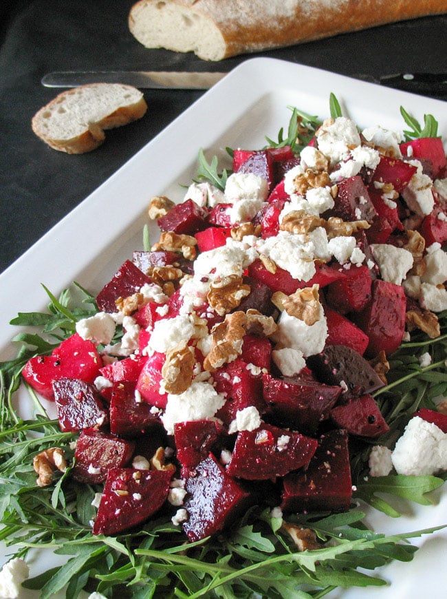 Roasted Beetroot Salad, with Goats Cheese & Walnuts arranged on a white platter with a loaf of French bread in the background. .