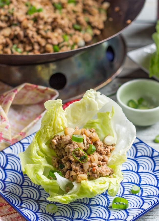 A single lettuce cup, filled with San Choy Bow mixture, sitting on a blue and white Chinese patterned plate. 