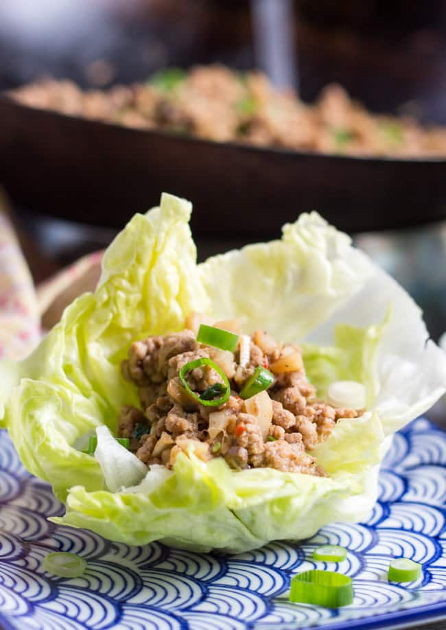 A close up shot of a lettuce cup filled with san choy bow mixture, with a wok of the mixture in the background.  