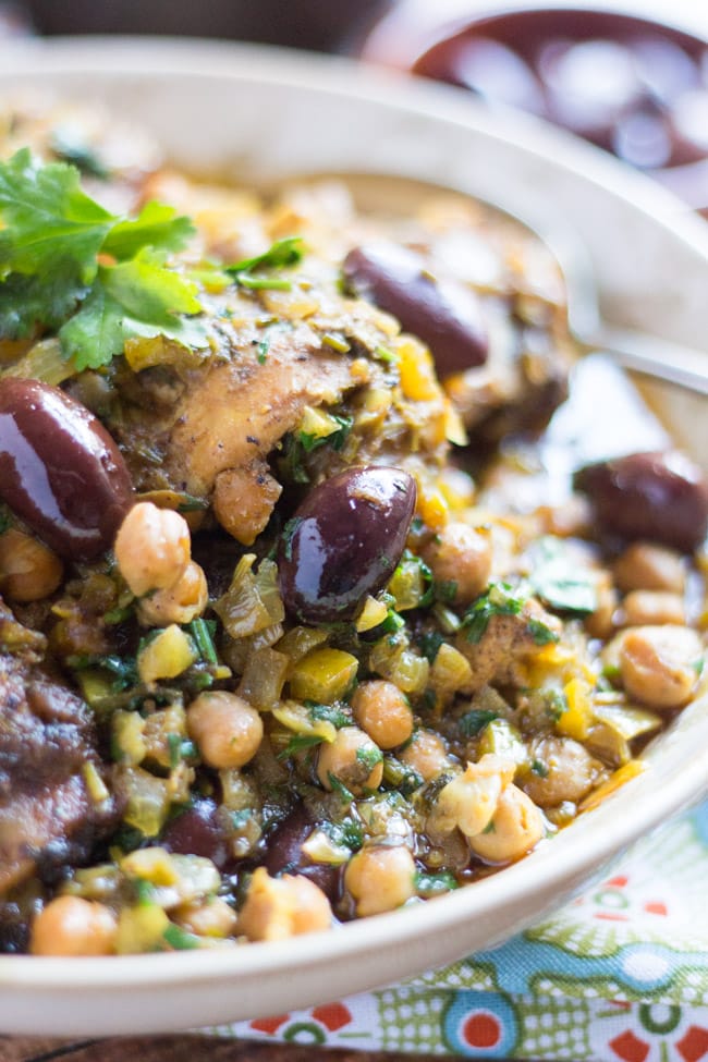 A close up shot of a bowl of Slow Cooker Moroccan Chicken Tagine, with four black kalamata olives, chickpeas and pieces of preserved lemon. 