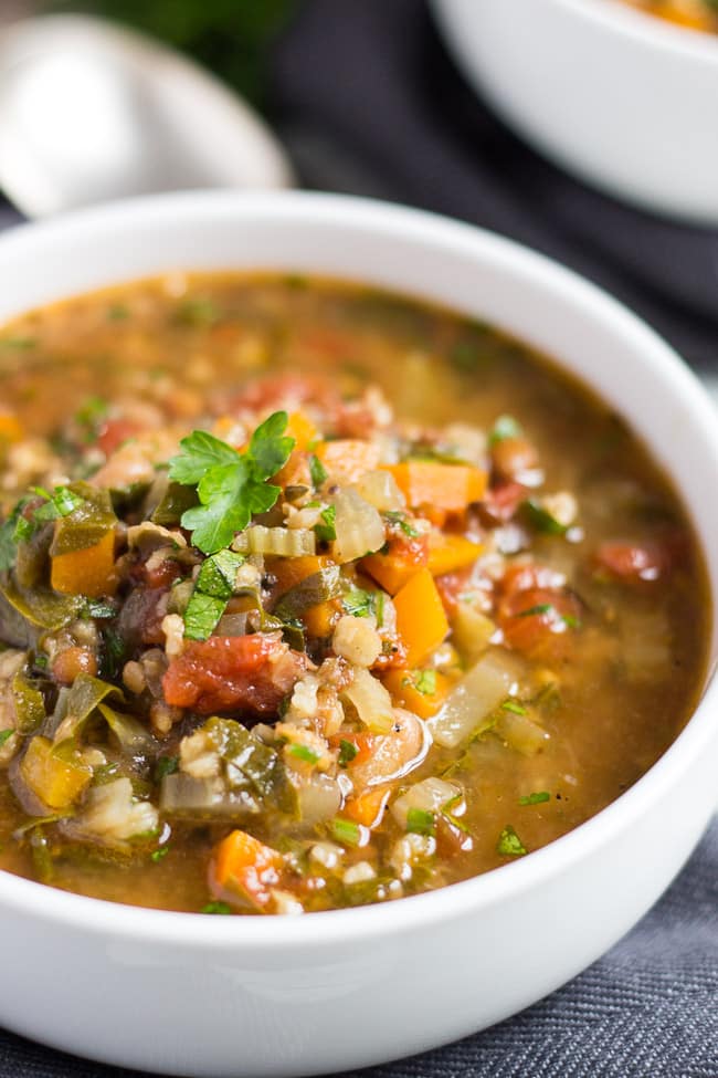 A close up shot of a white bowl of slow cooker vegetable soup made with soup mix showing the chopped vegetables and cooked grains.