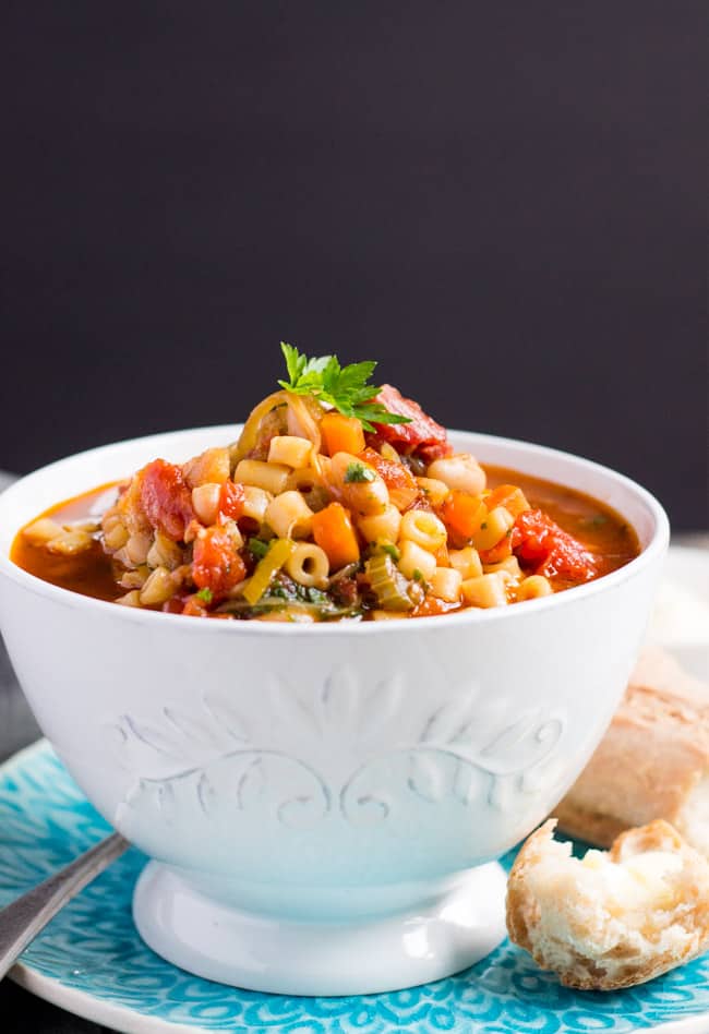 A side on shot of a white bowl of easy minestrone soup with some crusty bread on the side.