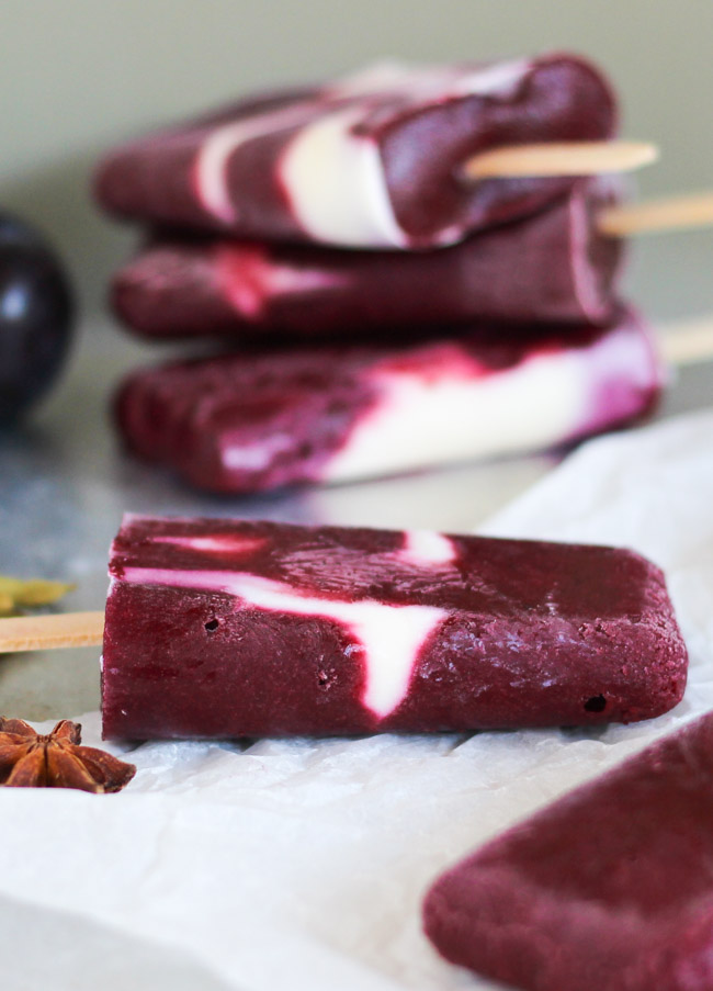 A single spiced plum & yoghurt popsicle on a sheet of baking paper, with a stack of yoghurt popsicles in the background. 