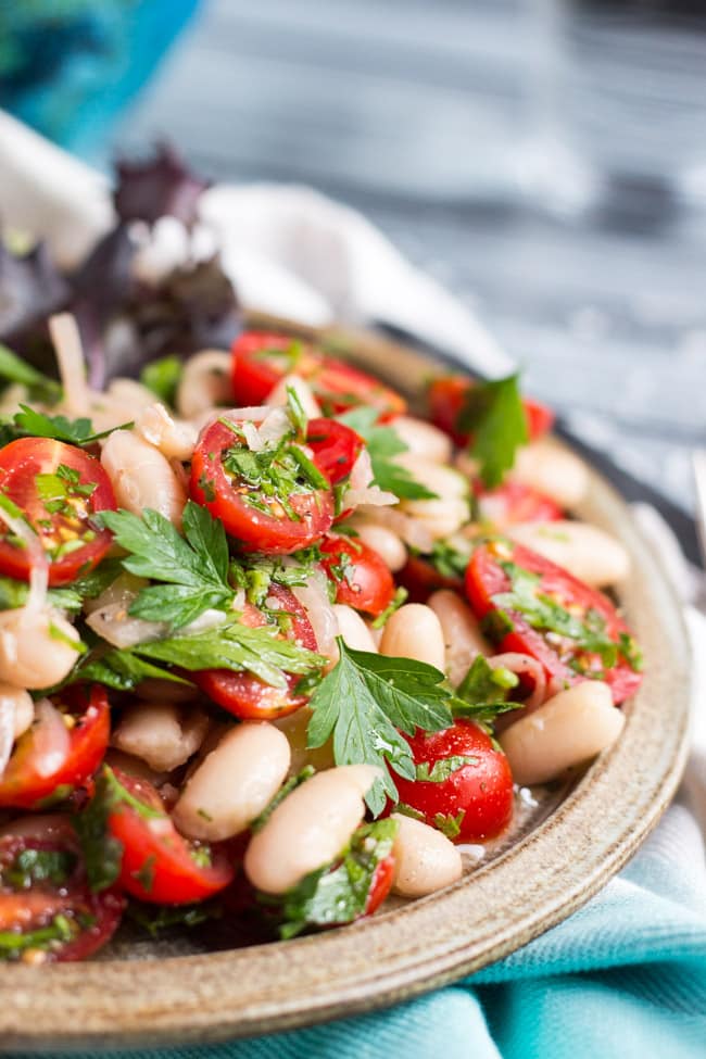 A close up shot of tomato & white bean salad on a brown plate. 