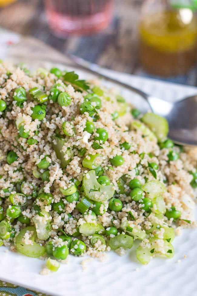 A large pile of couscous salad, flecked with slices of celery and cooked green peas.