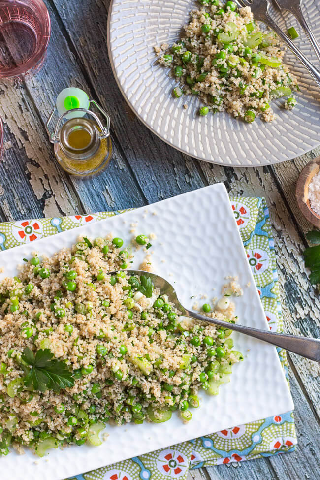 A silver spoon digs into a pile of vegetable couscous salad, which is piled onto a white platter.